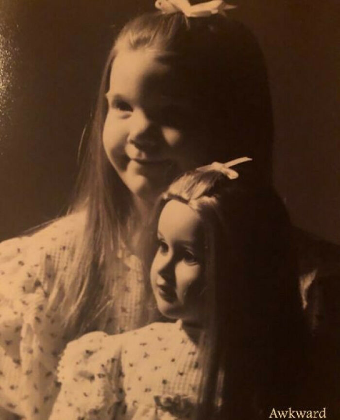 Young girl and doll dressed alike in a vintage style photo, capturing an awkward family moment that feels incredibly sweet.