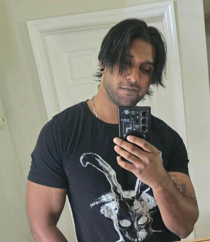 Man with fierceflow beautiful hair taking a mirror selfie, wearing a black graphic t-shirt with tattoos visible.