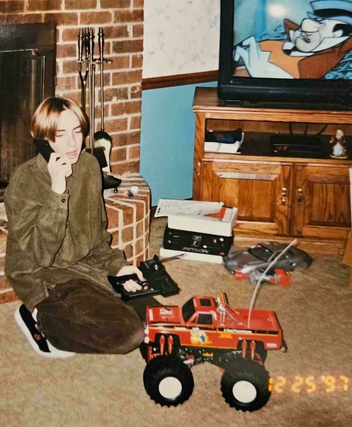 Young person on a phone call next to a toy truck, with TV cartoon showing, capturing '90s nostalgia.