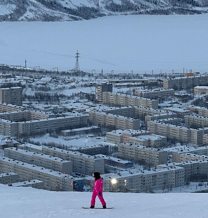 Snowboarder in pink suit in front of snow-covered urban buildings, illustrating an urban hellscape.