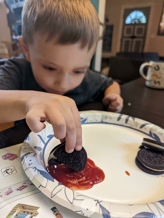 Un niño haciendo una tontería divertida: sumerge una galleta Oreo en salsa de tomate.