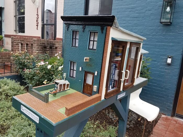 A mini house library in front of a blue building, featuring cool products with surprises inside.