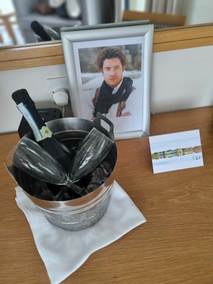 Champagne in an ice bucket with glasses next to a framed photo, capturing a funny wholesome anniversary surprise setup.