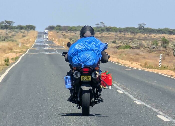 Motorcyclist travels down an empty Australian road with camping gear and supplies.