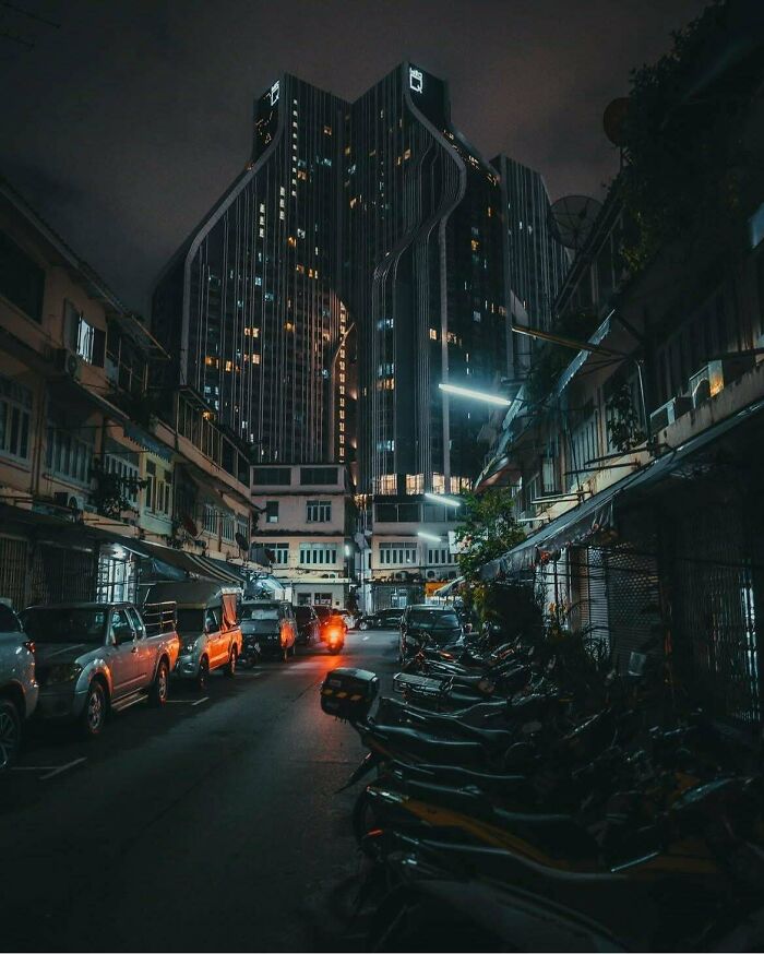 Dark city street at night with a towering building emanating an evil aura like a supervillain headquarters.