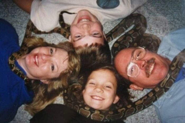 Family lying on the floor with a large snake draped around their necks in an awkward but sweet family photo moment.