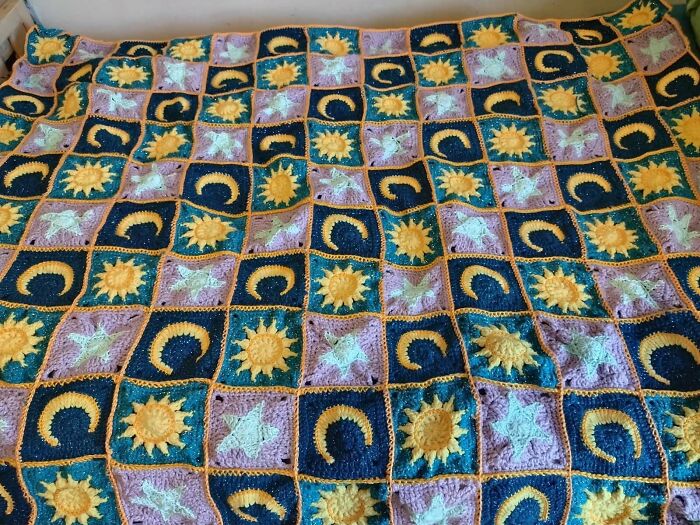 Colorful crochet blanket with sun, moon, and star patterns proudly displayed by crochet enthusiasts.