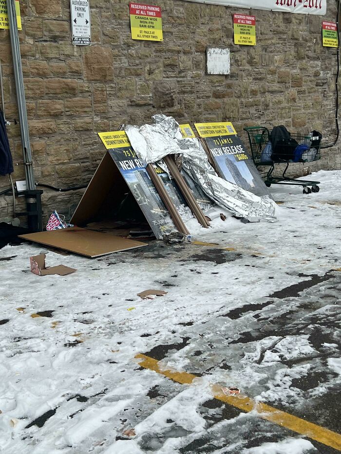 Temporary shelter made from promotional posters in a snowy parking lot, hinting at a boring dystopia.