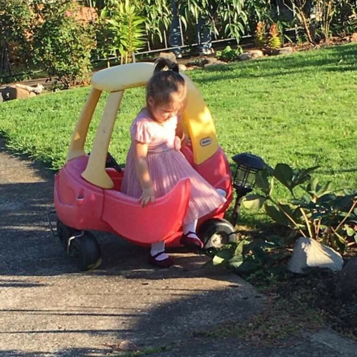 Child hilariously stuck in a toy car in a garden, capturing a funny childhood moment.