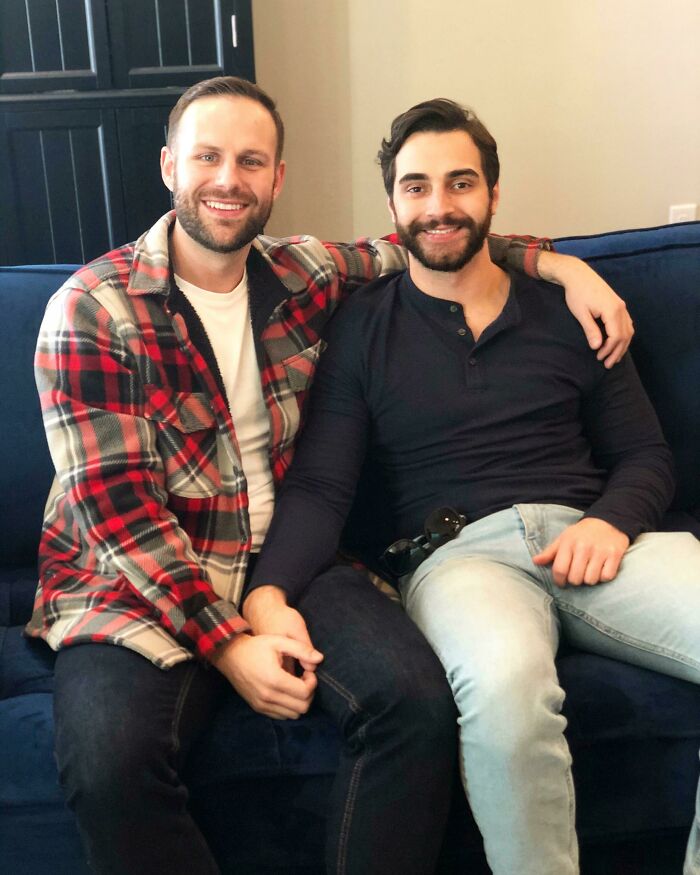 Two men sitting on a couch, embracing and smiling, showcasing long-distance love.