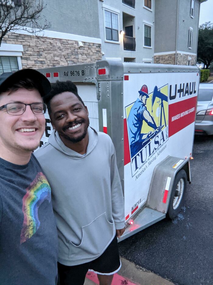Two friends smiling next to a U-Haul trailer, showcasing a joyful long-distance moving moment.