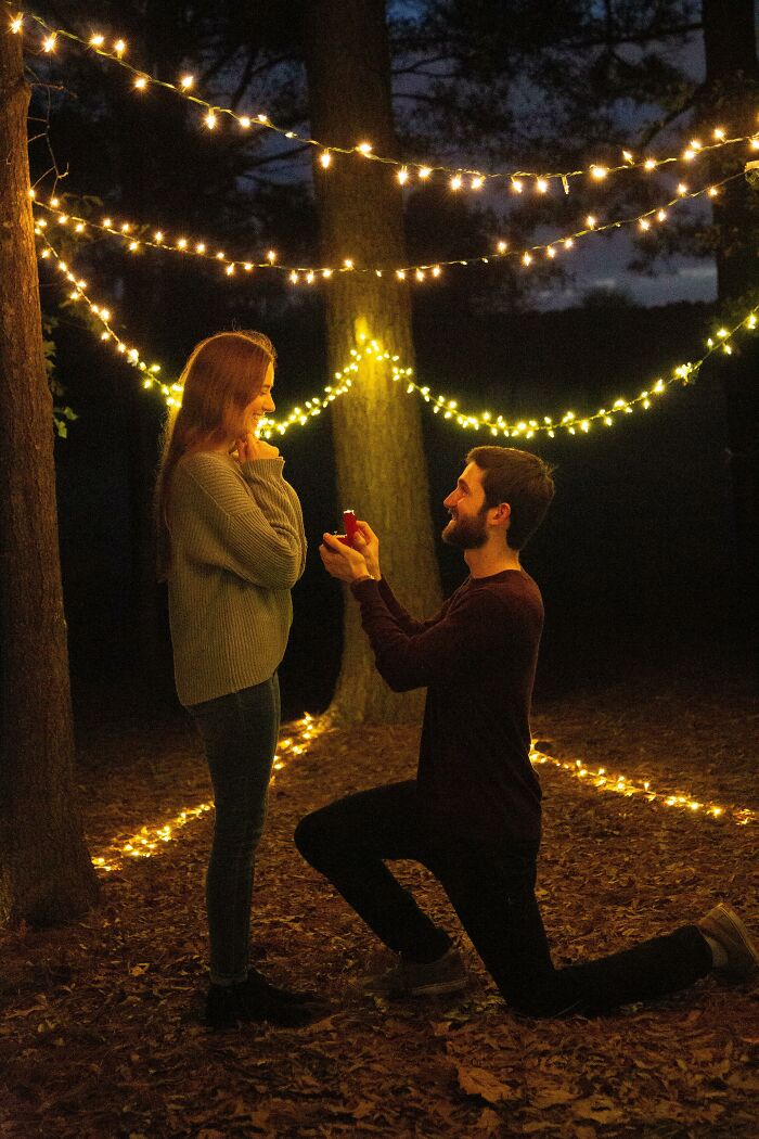 Man proposing to woman under string lights in a forest, symbolizing love overcoming distance.