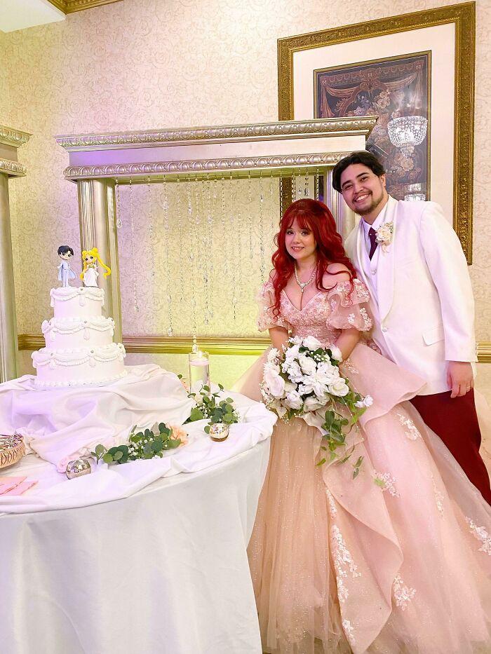 A couple in wedding attire stands smiling beside a decorated cake, symbolizing long-distance love triumphing.