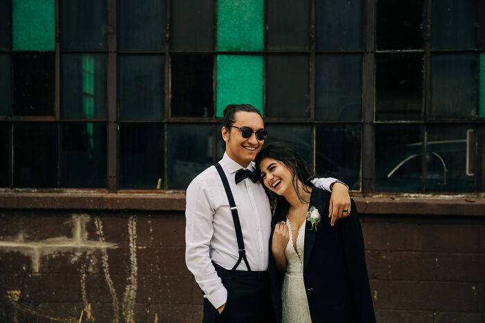 A couple embracing and smiling, showing love in front of an industrial window backdrop.