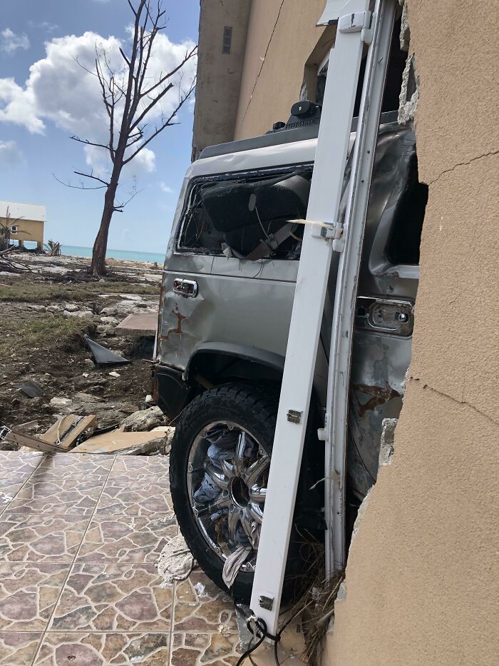 Damaged car lodged in a building wall after a storm, illustrating nature disaster resilience challenges.