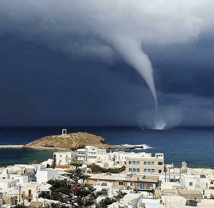 Waterspout forming over the sea near coastal town, illustrating nature disaster resilience amidst stormy conditions.