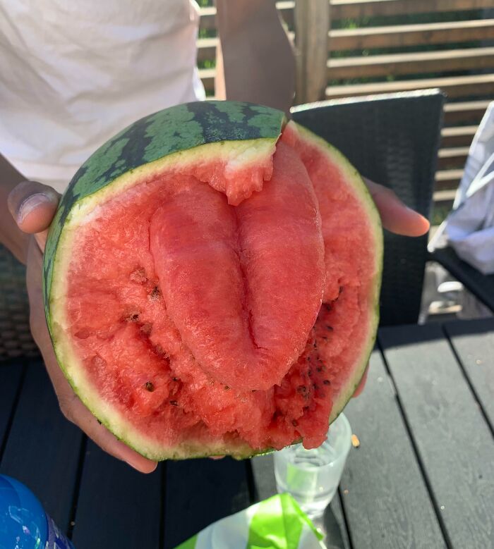 A sliced watermelon showing pareidolia, resembling a mouth or face, held by a person over a table.