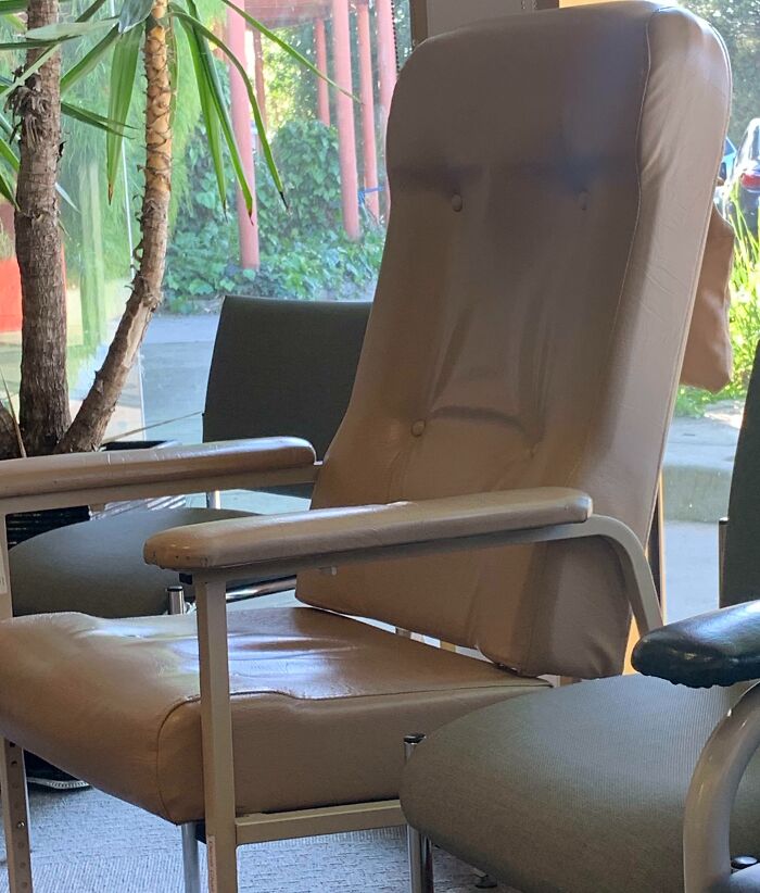 Chair in a waiting room, its pattern resembling a face, showcasing pareidolia with plant in the background.