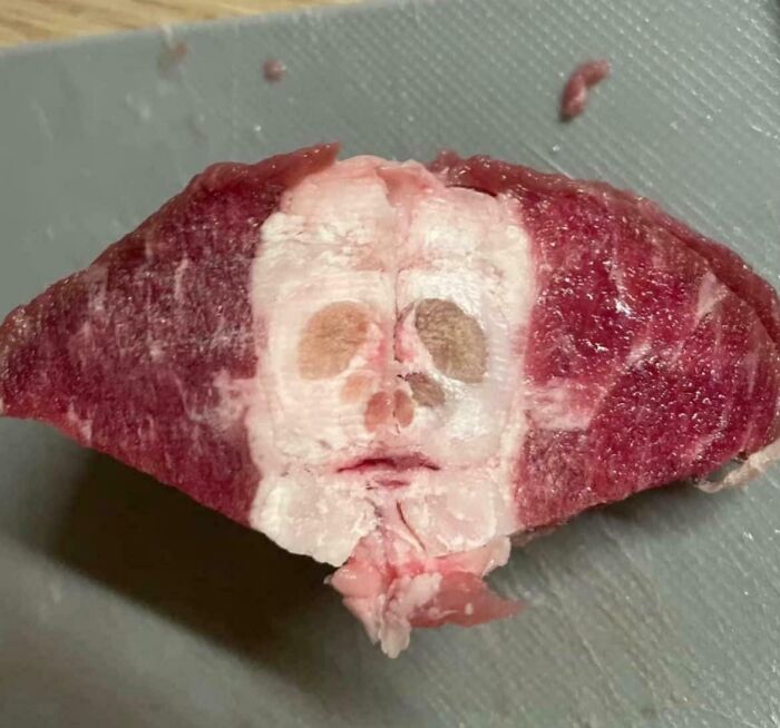 A piece of meat resembling a face, showcasing pareidolia, placed on a cutting board.