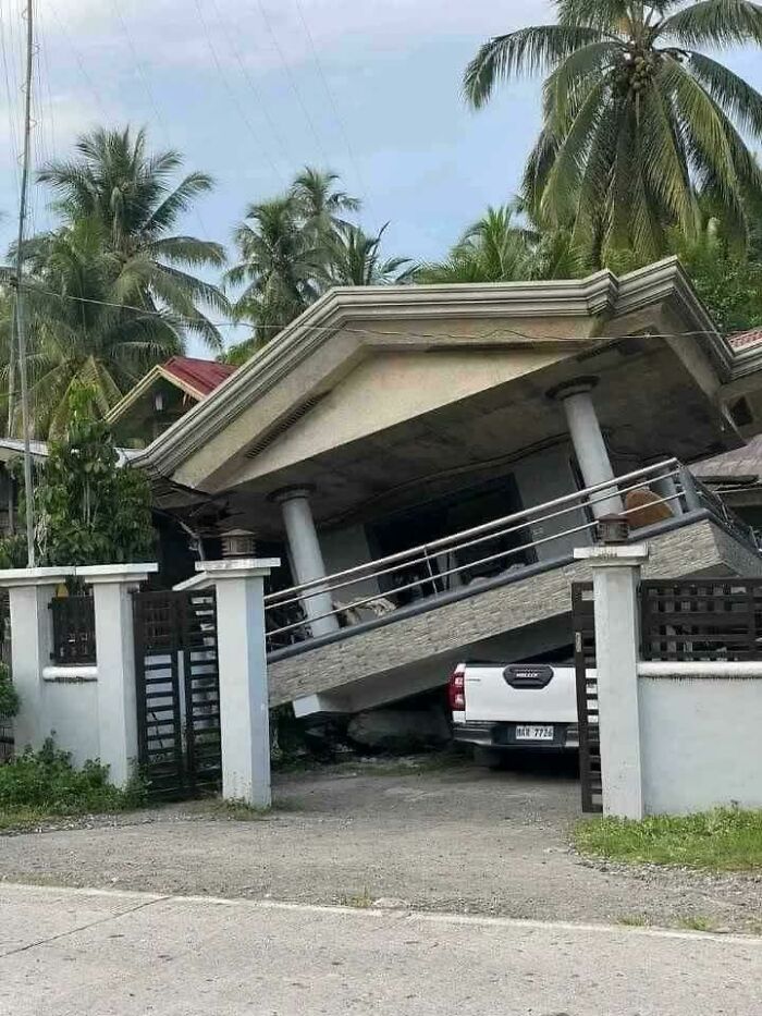 Collapsed house with a car underneath, highlighting nature disaster resilience challenges amidst tropical vegetation.
