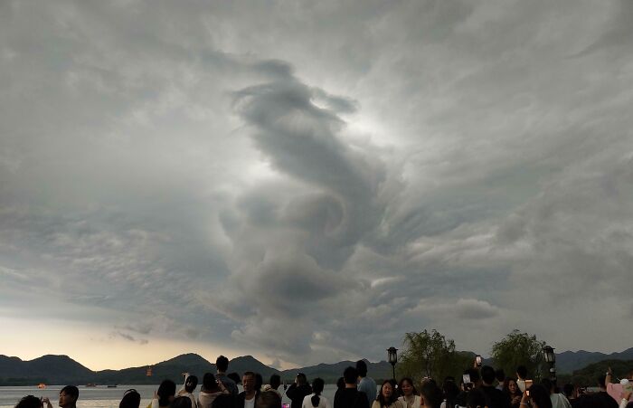 Cloud formation resembling a face, capturing pareidolia, with a crowd of people observing in the foreground.