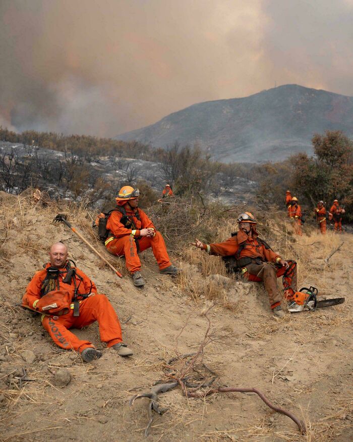 Firefighters in orange suits resting during wildfire, showcasing nature disaster resilience efforts in challenging conditions.