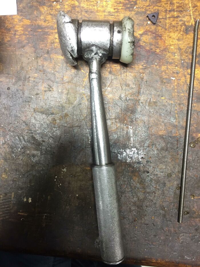 A worn-down hammer with a textured metal handle, illustrating the effects of time and use, lying on a scratched workbench.