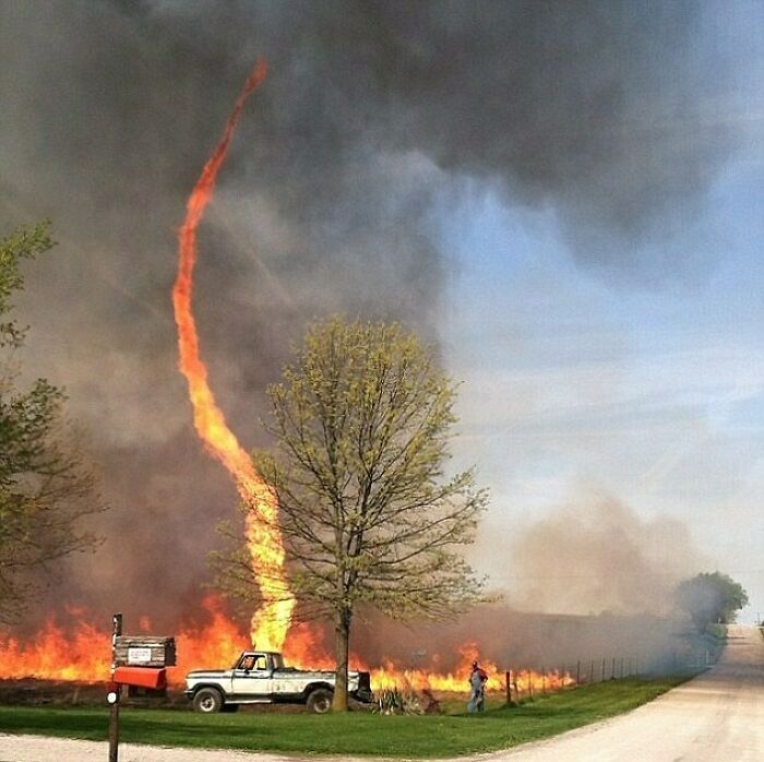 Fire tornado in a field, illustrating nature disaster resilience with a truck and person nearby amidst smoke and flames.