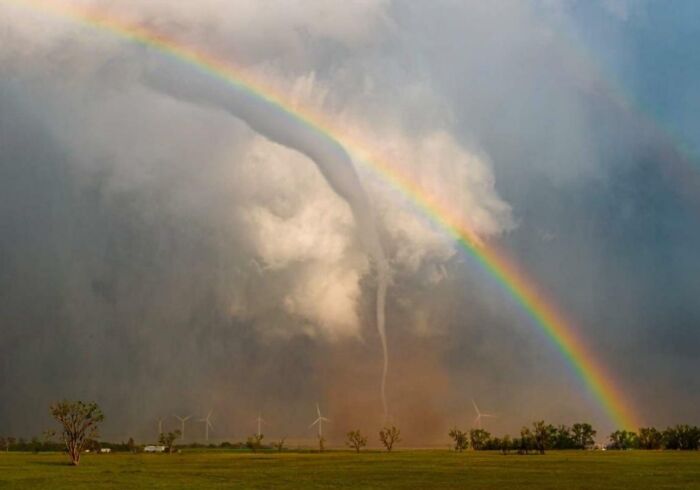 Tornado meets a rainbow over a field with wind turbines, illustrating nature disaster resilience.