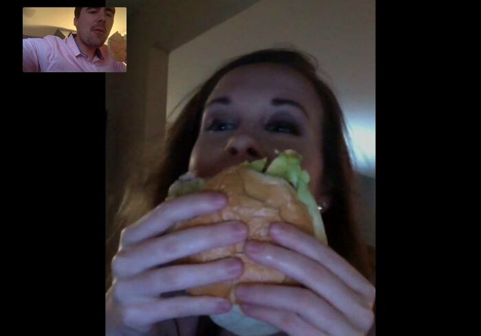 Woman eating a burger during a video call, illustrating long-distance love.