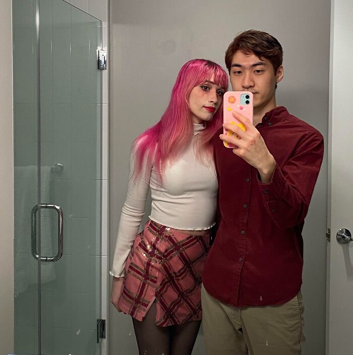 A couple in a bathroom mirror selfie, showcasing long-distance love, with the woman in a plaid skirt and the man in a burgundy shirt.
