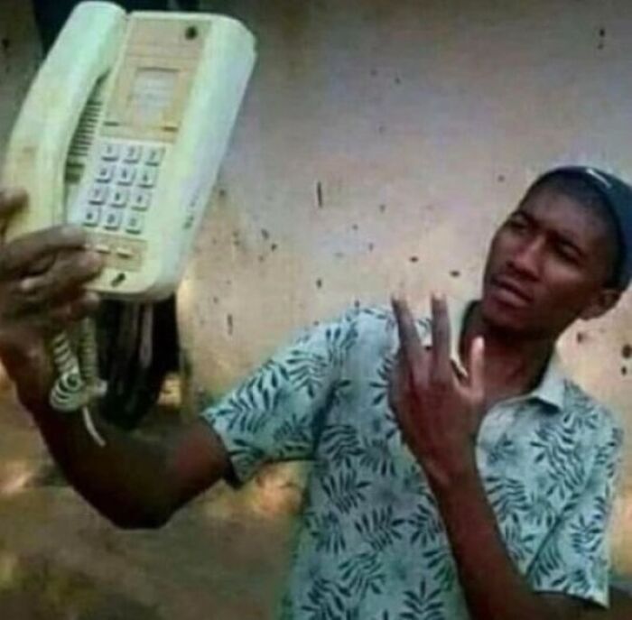 Hombre sosteniendo un teléfono antiguo y haciendo un gesto confundido en imagen que genera risas en internet.