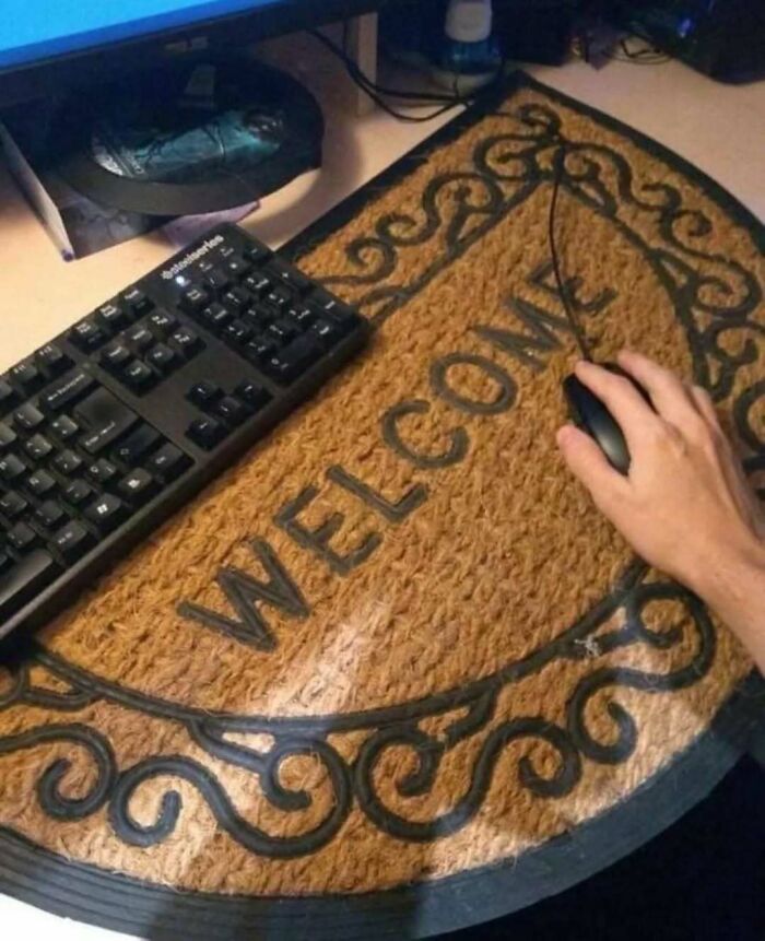 Hand using computer mouse on a welcome doormat next to a keyboard, showcasing random photos for processing.