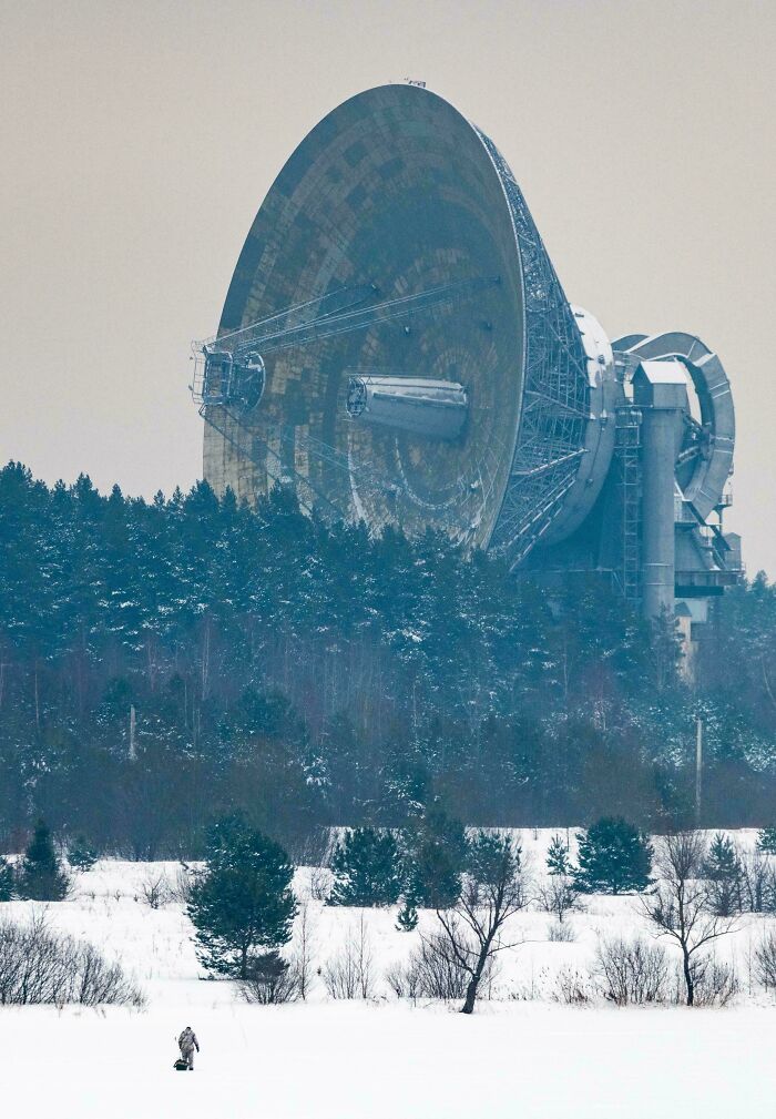 Massive satellite dish towering over snowy landscape and tiny person, illustrating the concept of megalophobia with scarily big scale.