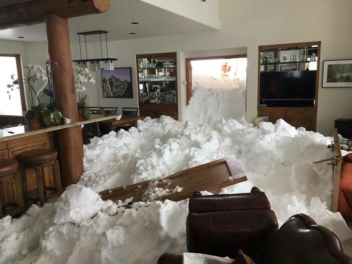 Indoor snowstorm aftermath showing nature-disaster-resilience, with snow piling into a living room through an open door.