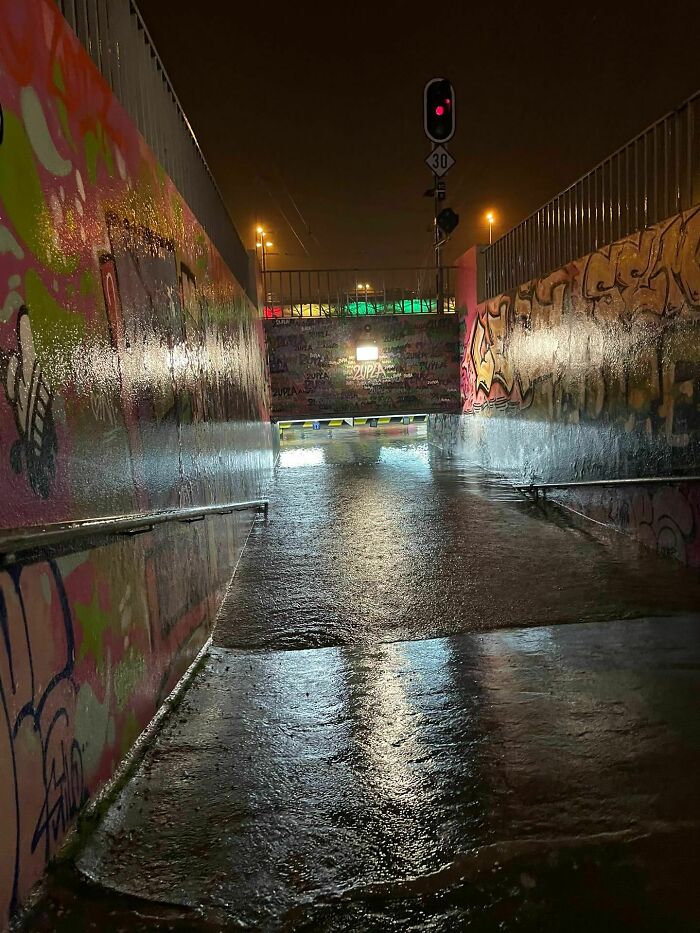 Flooded underpass at night with graffiti walls and traffic lights highlighting nature disaster resilience.
