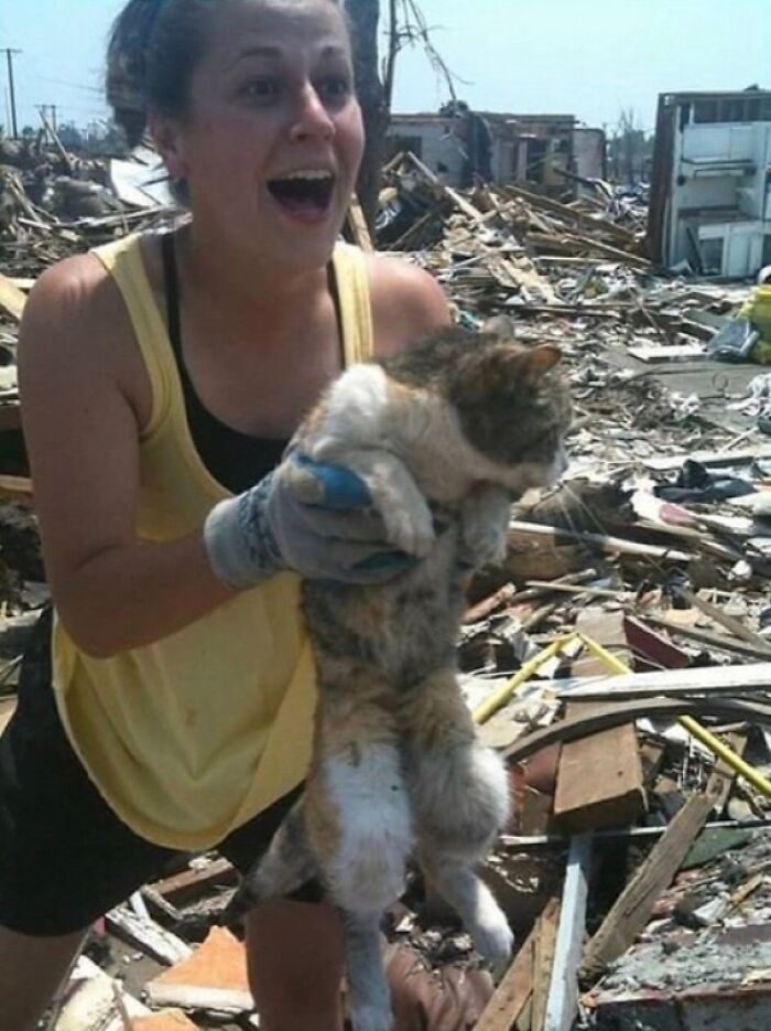 Woman joyfully rescuing a cat from debris, showcasing nature disaster resilience.