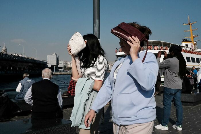 People using bags to shield their faces in a street photography scene by the water.
