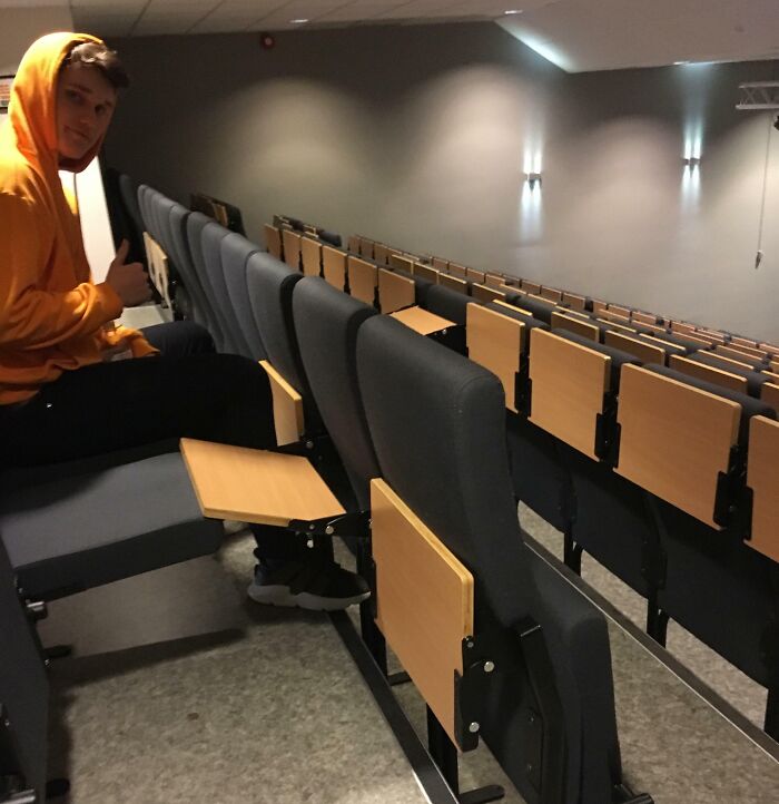 A person in a hoodie gives a thumbs up in a poorly designed lecture hall with obstructed desks.