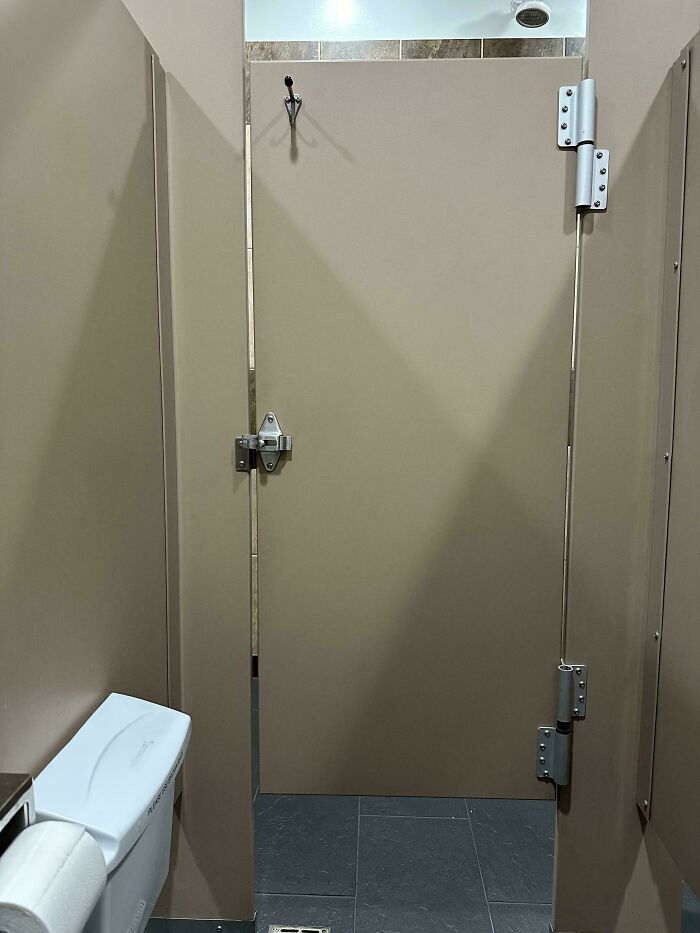 Public restroom stall with large gap in door, showcasing unfortunate design.