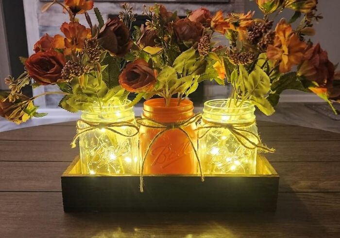 Mason jars with flowers and fairy lights create dopamine decor on a wooden table.