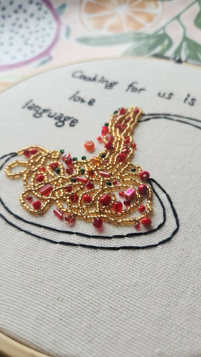 Close-up of beautiful embroidery design featuring gold and red beads on fabric with stitched text about love and cooking.