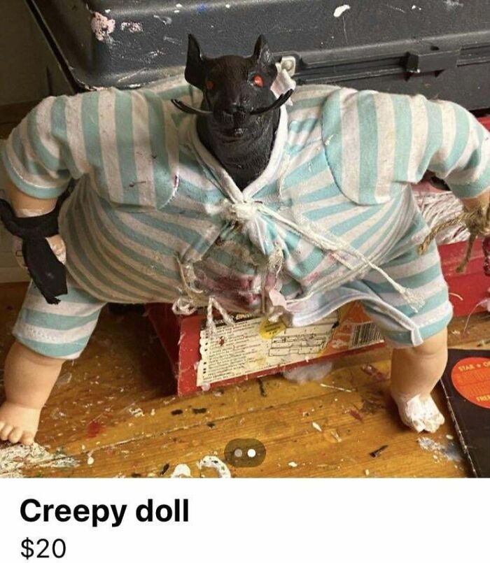 Creepy doll with a dark animal head, striped clothes, sitting on a wooden surface.