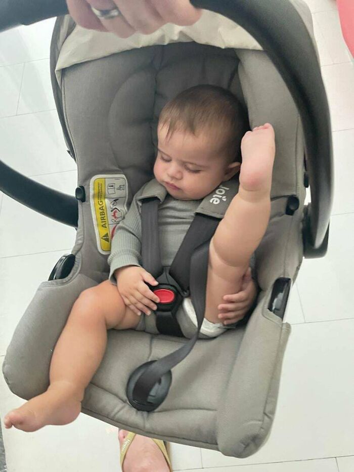 Baby comfortably sitting in a car seat with a raised leg, showing a wholesome dad moment.