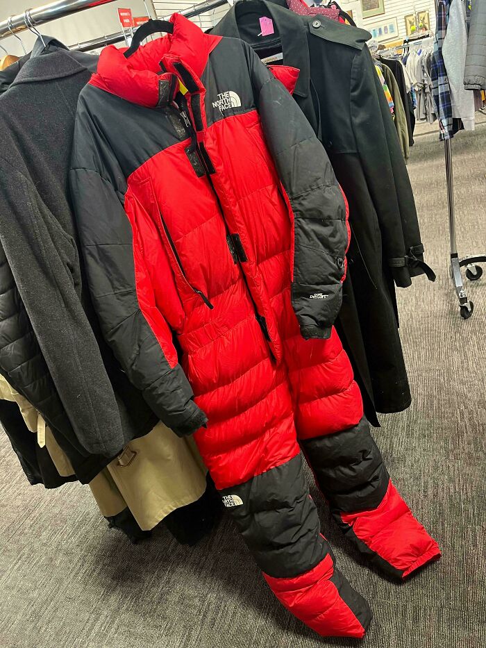 Red and black North Face jumpsuit hanging in a thrift store among other coats.