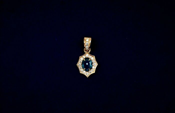 Gold and sapphire pendant on a dark background, a funny wholesome anniversary surprise.