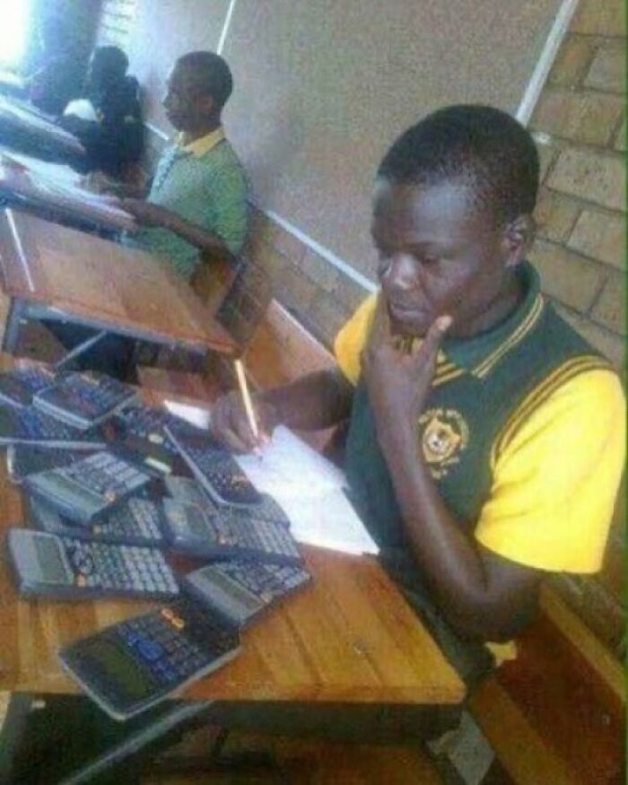 Student surrounded by multiple calculators, writing notes in a classroom setting showing the weird side of the internet.