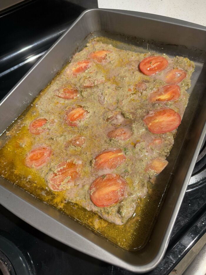 Unappetizing baked dish with tomatoes in a greasy, unappealing sauce in a metal pan, part of dumb dishes collection.