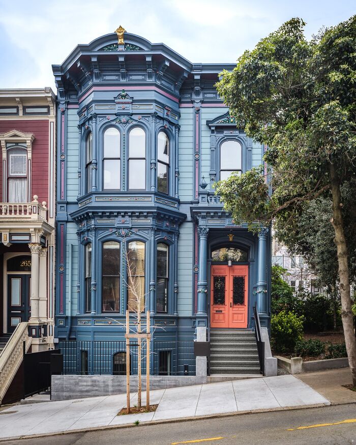 Victorian-style house painted in blue showcasing impressive architectural feats with detailed trim and coral front doors.