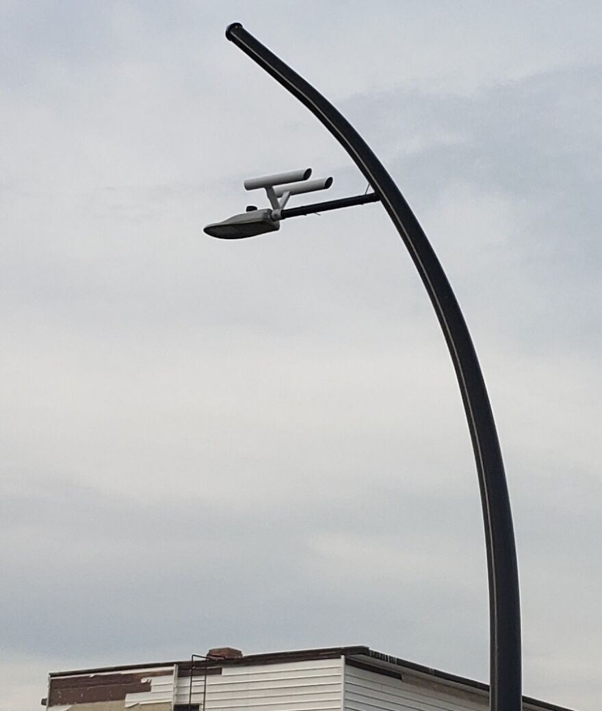 Streetlight shaped like an airplane, blending into an urban setting with buildings and a parked truck below.
